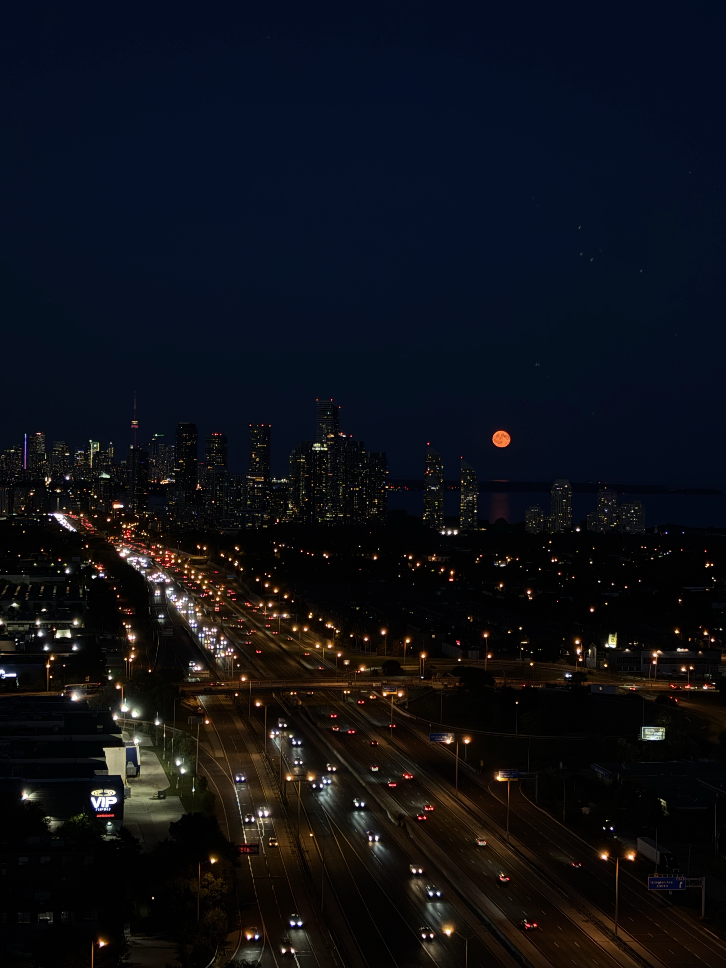 Toronto skyline at night with the moon above the lake.